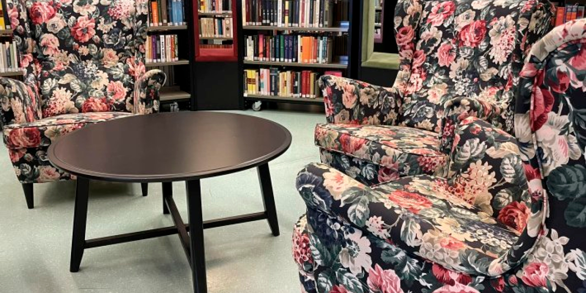 Nojatuoleja ja pöytä kirjahyllyjen keskellä.