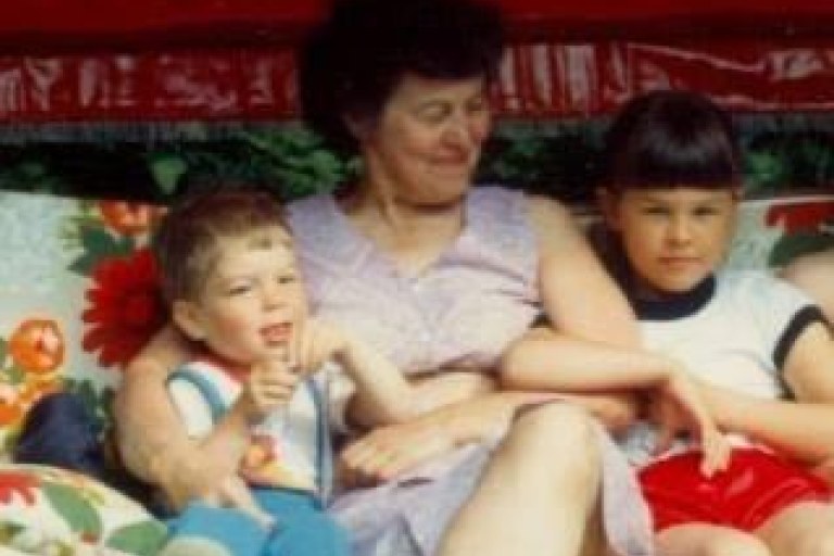 Nainen ja kaksi lasta istuvat värikkäässä pihakeinussa.
