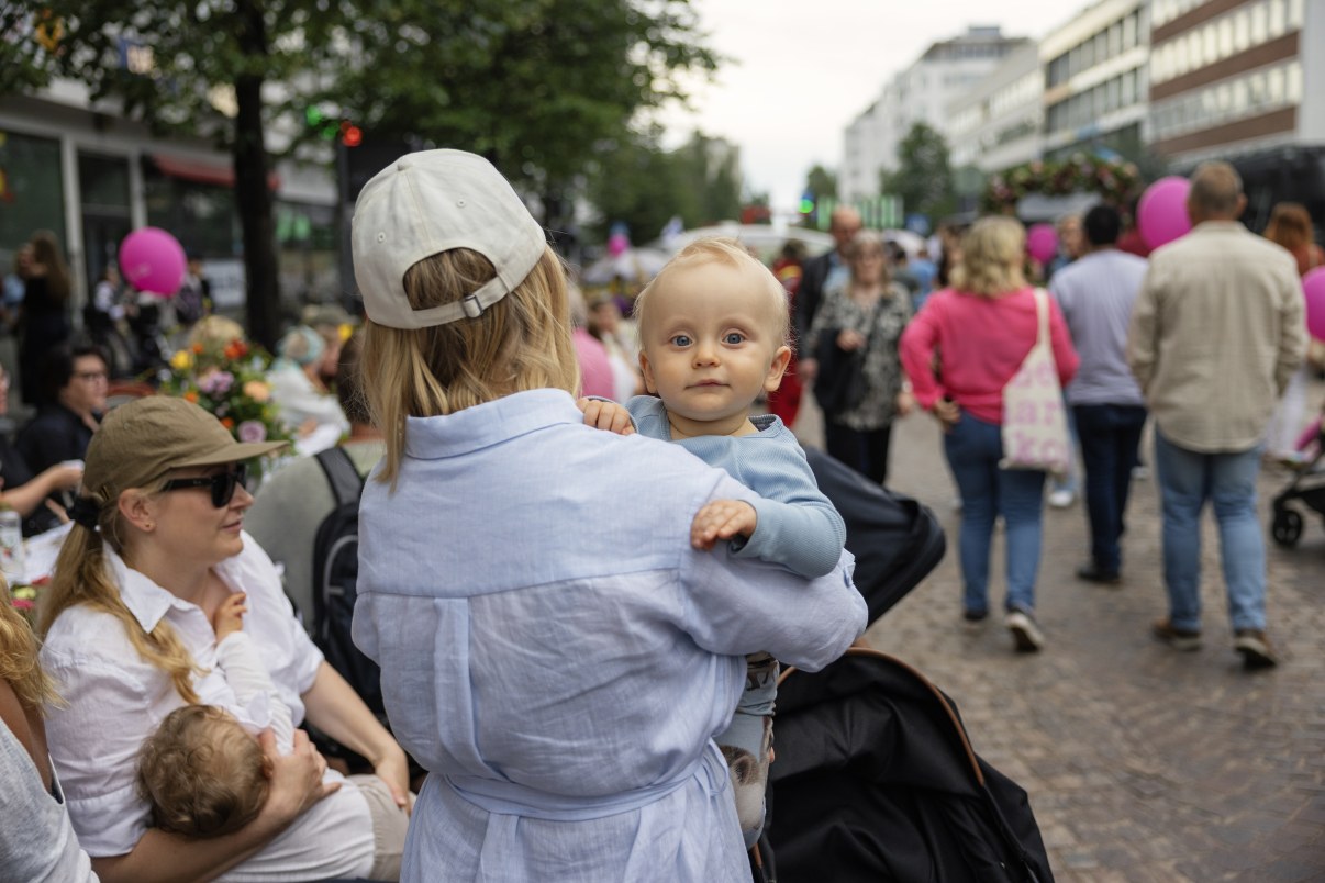 Kuvassa on äiti ja lapsi kadulla ihmisten ympäröimänä.