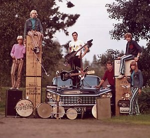 Porkkanas-yhtye rekvisiittanaan soittimia, vahvistimia ja auto.