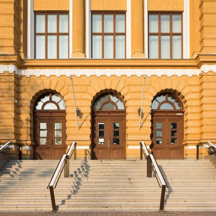 Picture of the City Hall entrance, there are yellow walls and three brown doors.