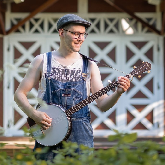 Mies pitää käsissään banjoa aurinkoisessa kesäsäässä