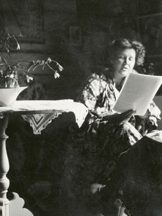 Vanha, mustavalkoinen valokuva, jossa Annikki Kariniemi lukee papereita pöydän ääressä.