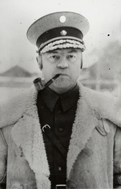 Vanha, mustavalkoinen valokuva, jossa K.M. Wallenius koppalakki päässä ja piippu suussa.