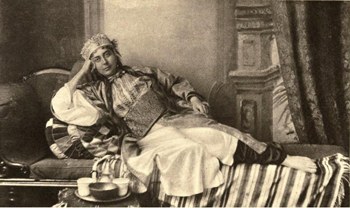 Vanha, mustvalkoinen valokuva naisesta makaamassa divaanilla.